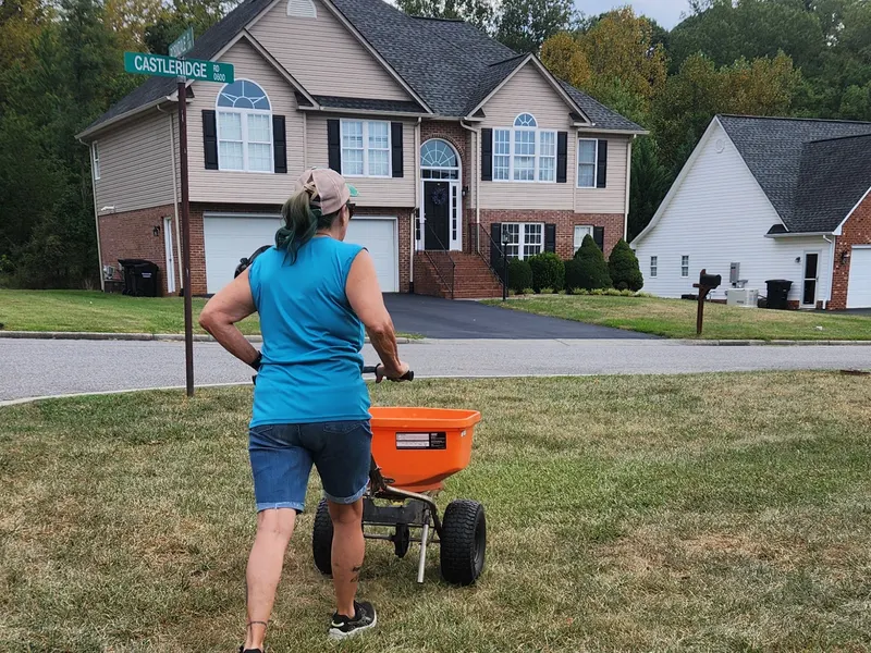 Theresa Terry spreading seed across a front lawn after aeration