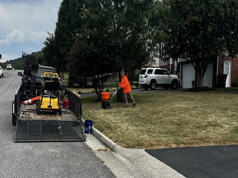 Aerator on the trailer at the curb while seed is spread on the lawn behind