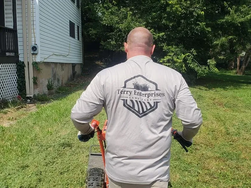 Terry Enterprises crew member running a walk-behind mower between two houses